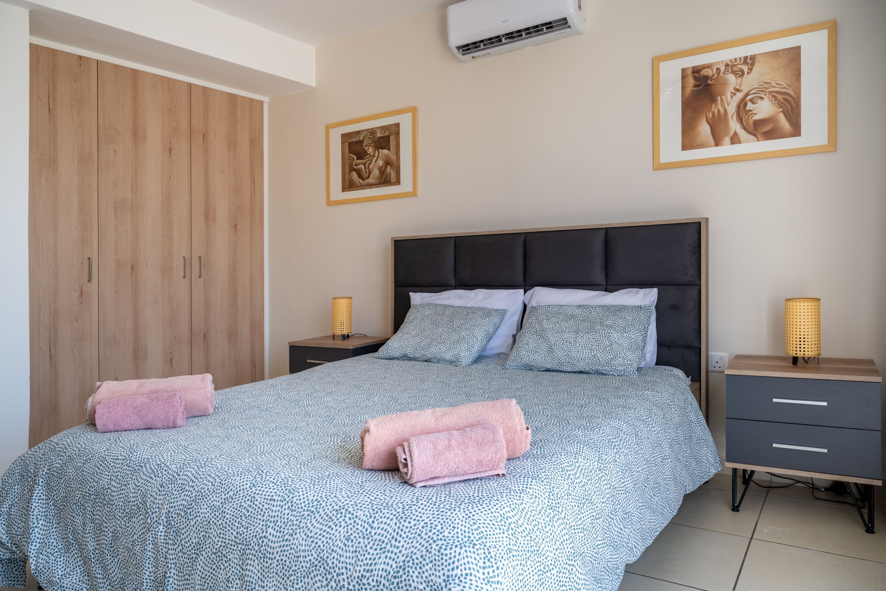 A bedroom with a bed, nightstands, a wardrobe, and wall art.