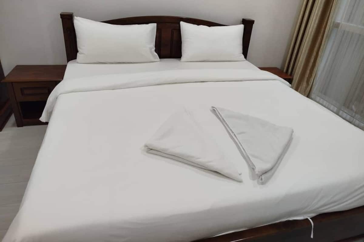 A neatly made bed with white linens and pillows, a wooden headboard, and a bedside table with a drawer.