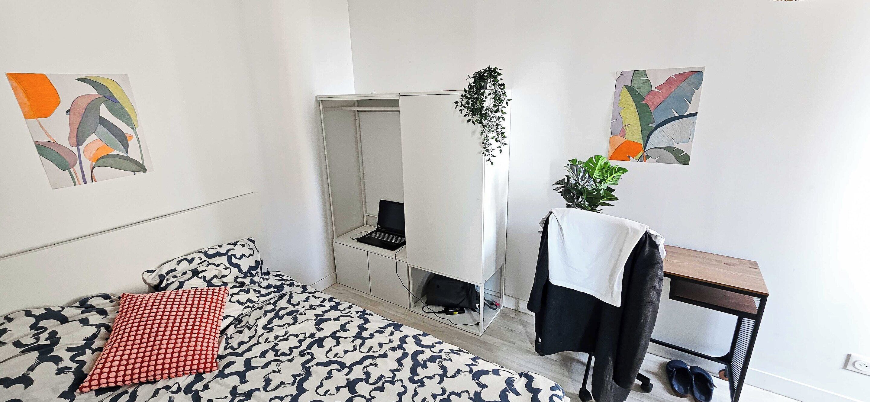 Een slaapkamer met een bed, een bureau, een stoel en een hangplant.