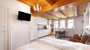 A bedroom with a large bed, a TV mounted on the wall, a dining area with a table and chairs, and a kitchen in the background. - Appartement Dijkzicht Near Schagen (Schagen)