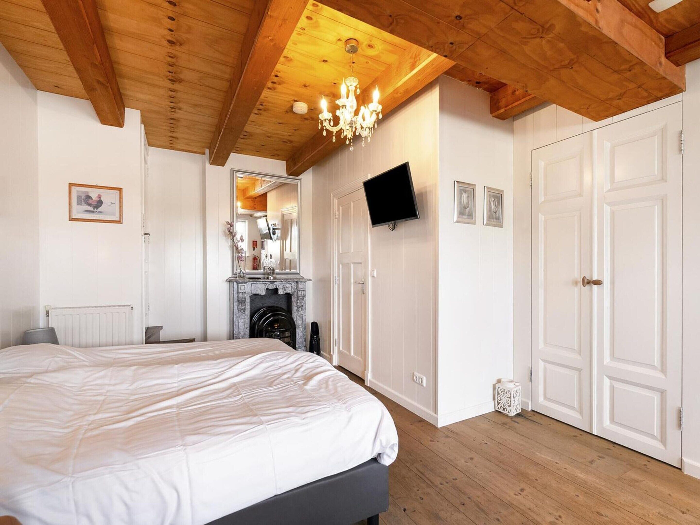 Une chambre avec un grand lit, une cheminée, une télévision et des portes blanches.
