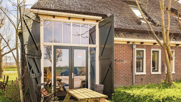 A wooden bench and a table in front of a house with a thatched roof and large windows. - Appartement Dijkzicht Near Schagen (Schagen)