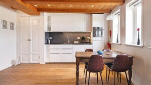 A modern kitchen with white cabinets, a wooden ceiling, and a dining area with a table and chairs. - Appartement Dijkzicht Near Schagen (Schagen)