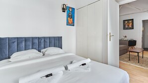 A modern hotel room with a large bed, a blue headboard, and a painting on the wall. - Charming 1 Bedroom Flat Heart of Marais (Paris)