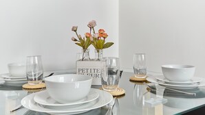A dining table set with white plates, bowls, and glasses, accompanied by a vase of flowers and a sign reading "PETITES FLEURS". - Charming 1 Bedroom Flat Heart of Marais (Paris)