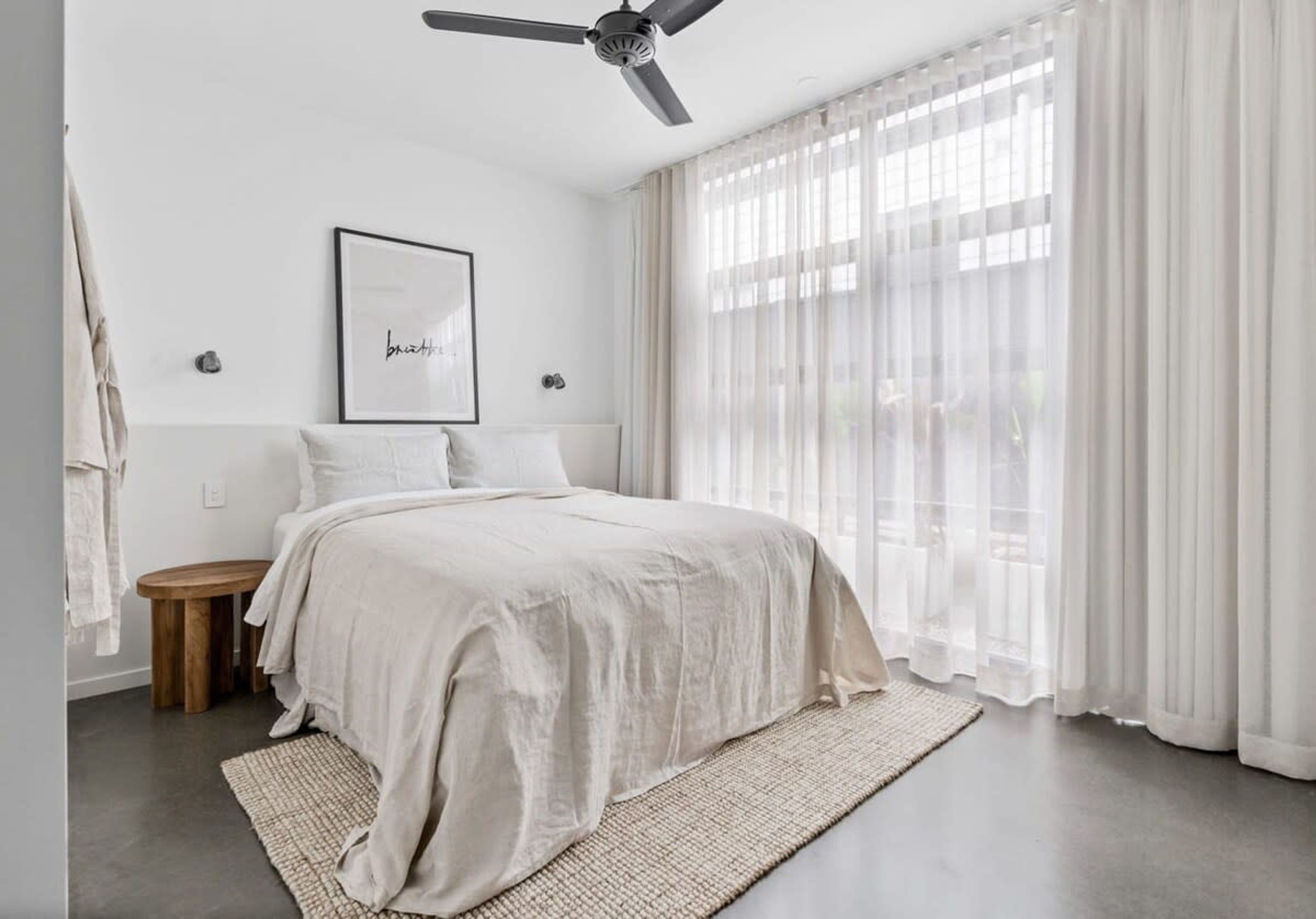 A bedroom with a bed, a ceiling fan, a framed picture, and sheer curtains.