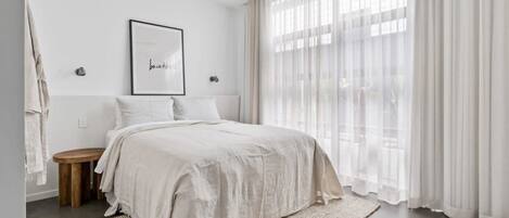 A bedroom with a bed, a ceiling fan, a framed picture, and sheer curtains.