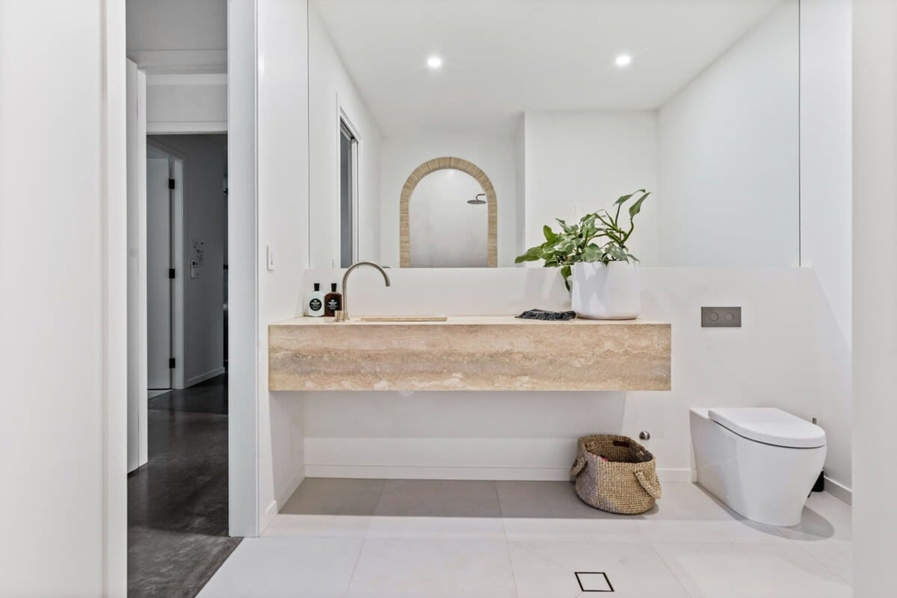 Un bagno moderno con un piano d'appoggio color beige, uno specchio grande, un lavabo, un water e una pianta.
