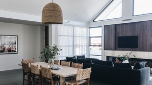 A modern living room with a dark sofa, wooden dining table, wicker chairs, and a large TV mounted on the wall. - Maple on Edward Berry - by Linnaeus Collection (Berry)