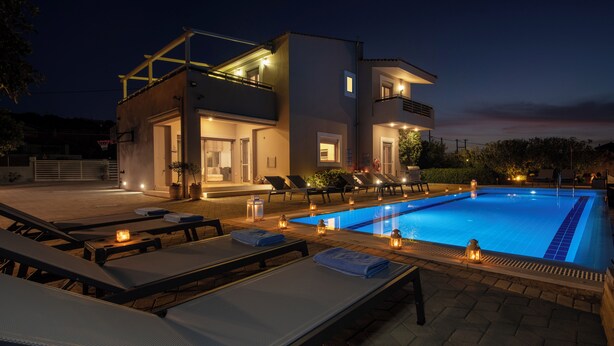 Un área moderna junto a la piscina con sillones de descanso y una pileta, rodeada por un edificio con varios balcones e iluminación exterior.