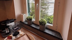 A modern kitchen with a large window, a coffee maker, a tea kettle, and a small potted plant on the windowsill. - Cappuccini's B&B (Livorno)
