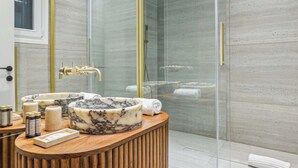 Un baño moderno con lavamanos de mármol, tocador de madera, cabina de ducha de vidrio y un espejo grande.