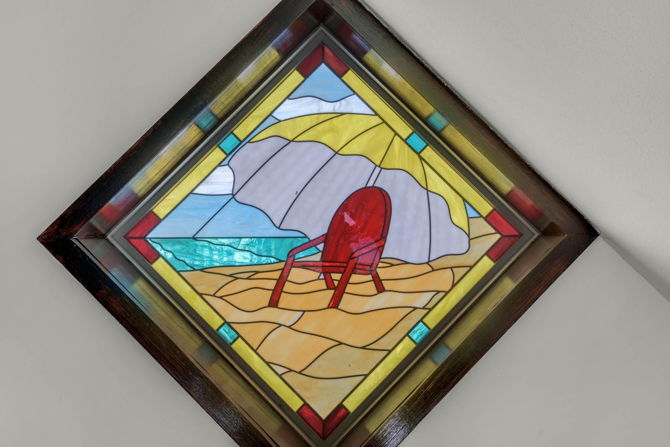 Una ventana de vitral con una escena de playa, que incluye una silla roja y un cuerpo de agua.