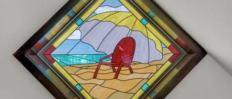 Una ventana de vitral con una escena de playa, que incluye una silla roja y un cuerpo de agua.