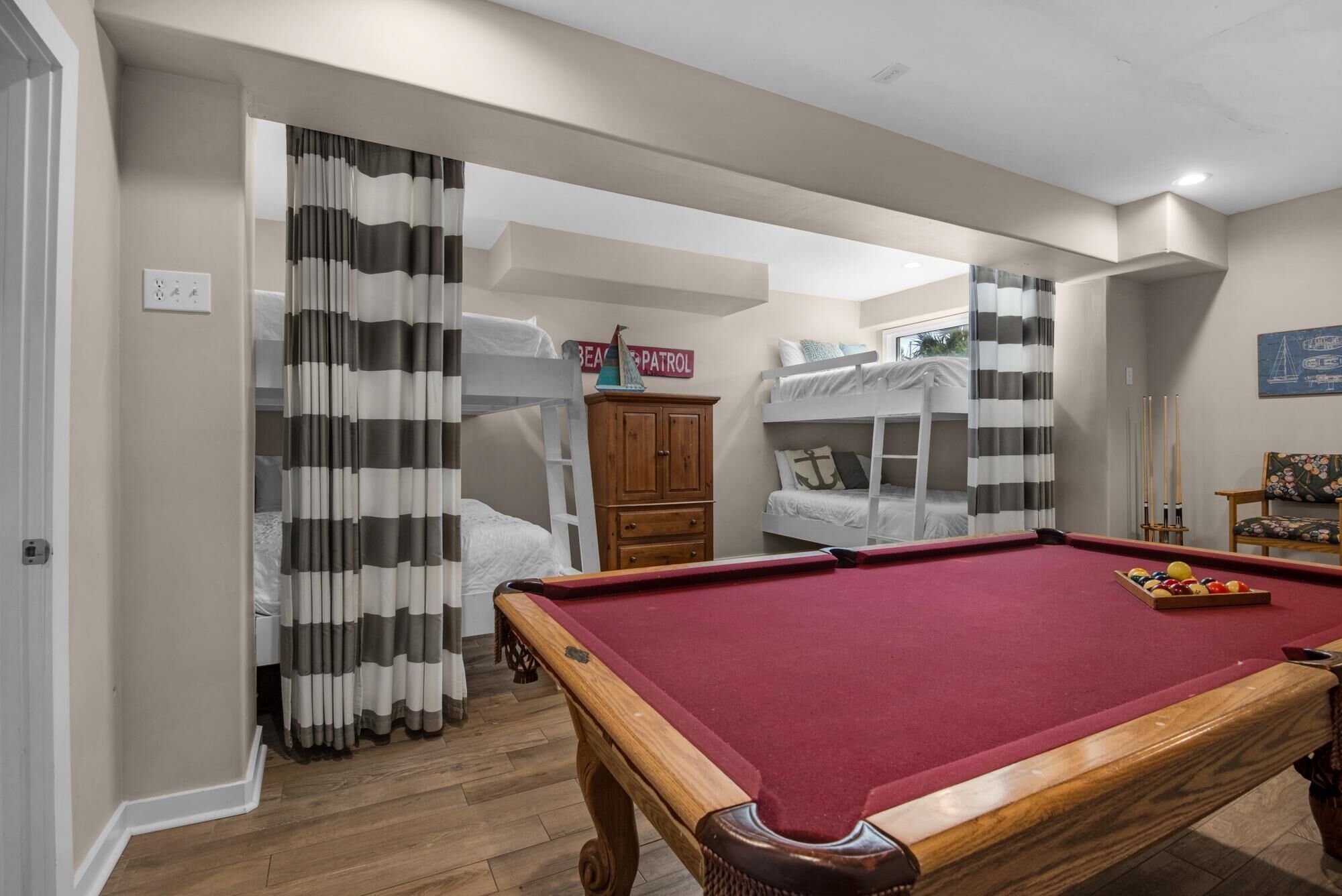 Een kamer met een pooltafel, stapelbedden, een houten kast en een bord waarop 'BEACH PATROL' staat.