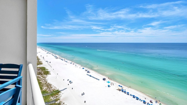 A beach view from a balcony with a clear sky, a sandy beach, and a calm sea. - Majestic Beach Towers 2-1608 (Panama City Beach)