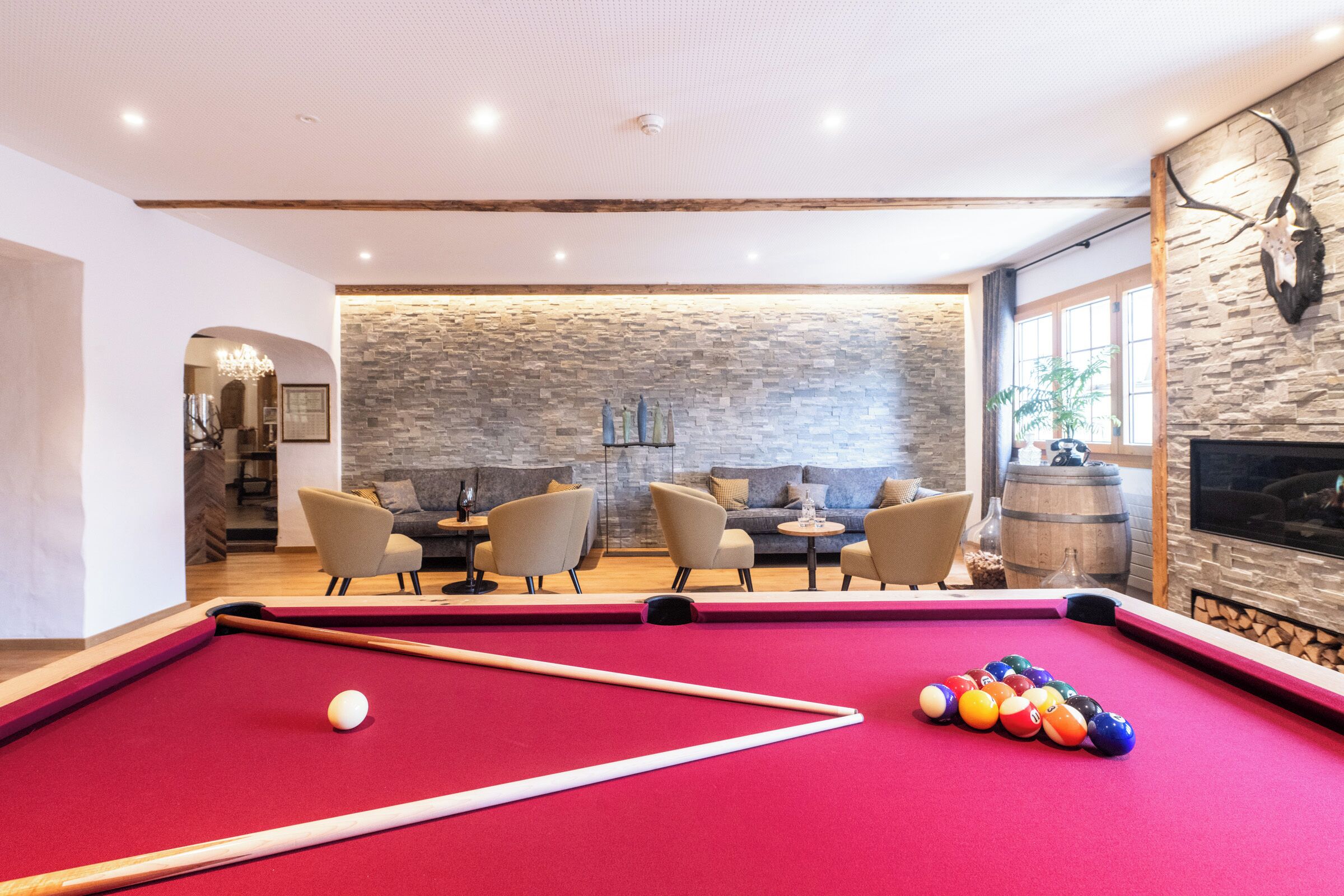 Una mesa de billar con bolas, un sofá y sillones en una habitación con paredes de piedra y techo de madera.