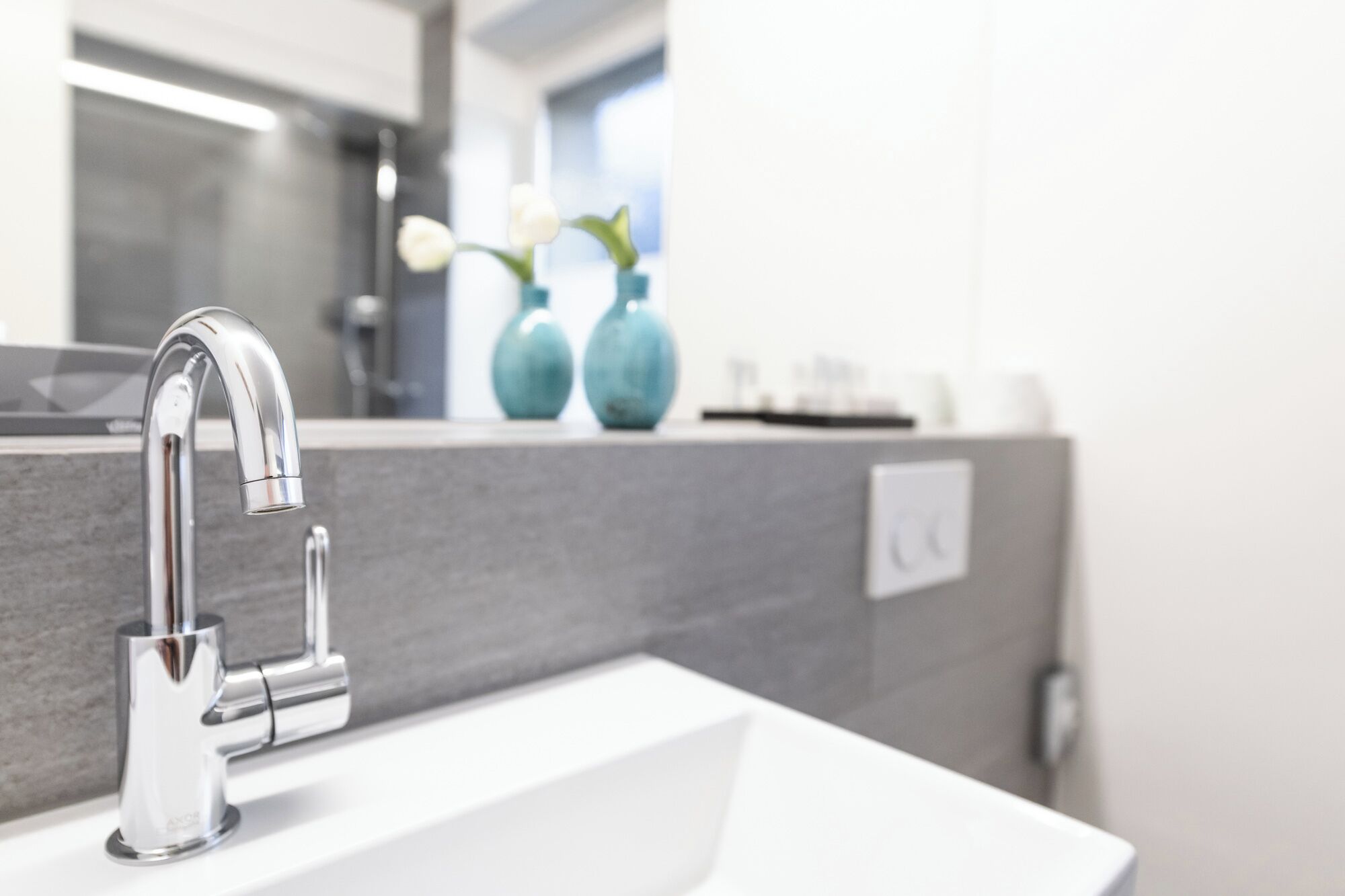 A modern bathroom with a chrome faucet, a white sink, and a mirror above it.
