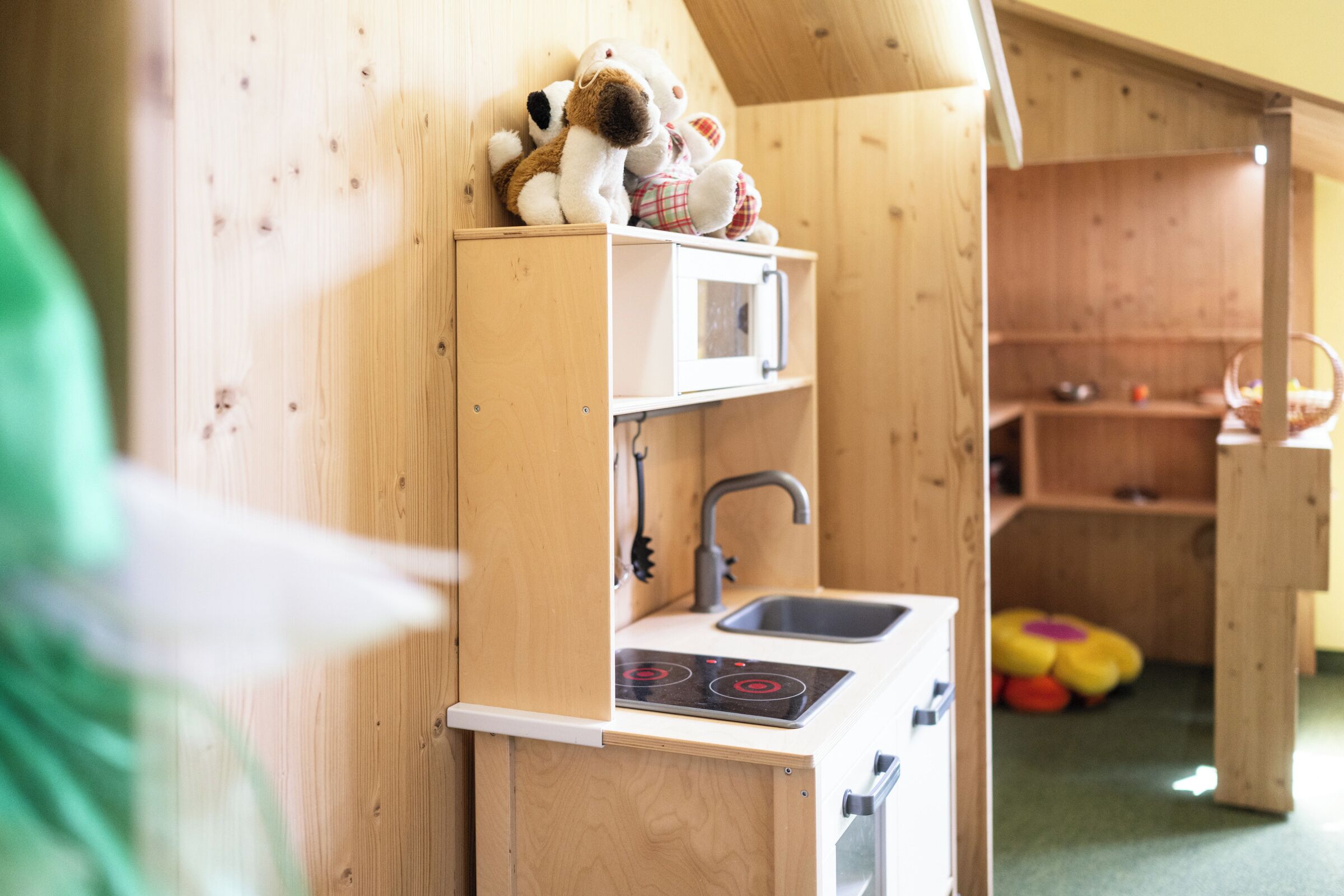 Een houten speelkeuken met een magnetron, gootsteen en fornuis.