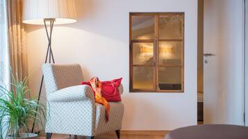 Ein Zimmer mit einem gemusterten Sessel, einer Stehlampe, einem Topfpflanzen und einem Fenster mit Milchglas.