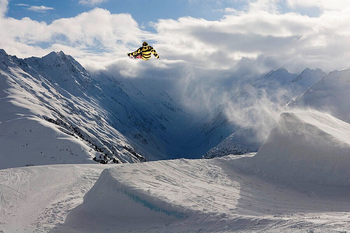 Un snowboarder en pleno vuelo sobre un paisaje montañoso cubierto de nieve.