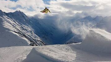 Un snowboarder en pleno vuelo sobre un paisaje montañoso cubierto de nieve.
