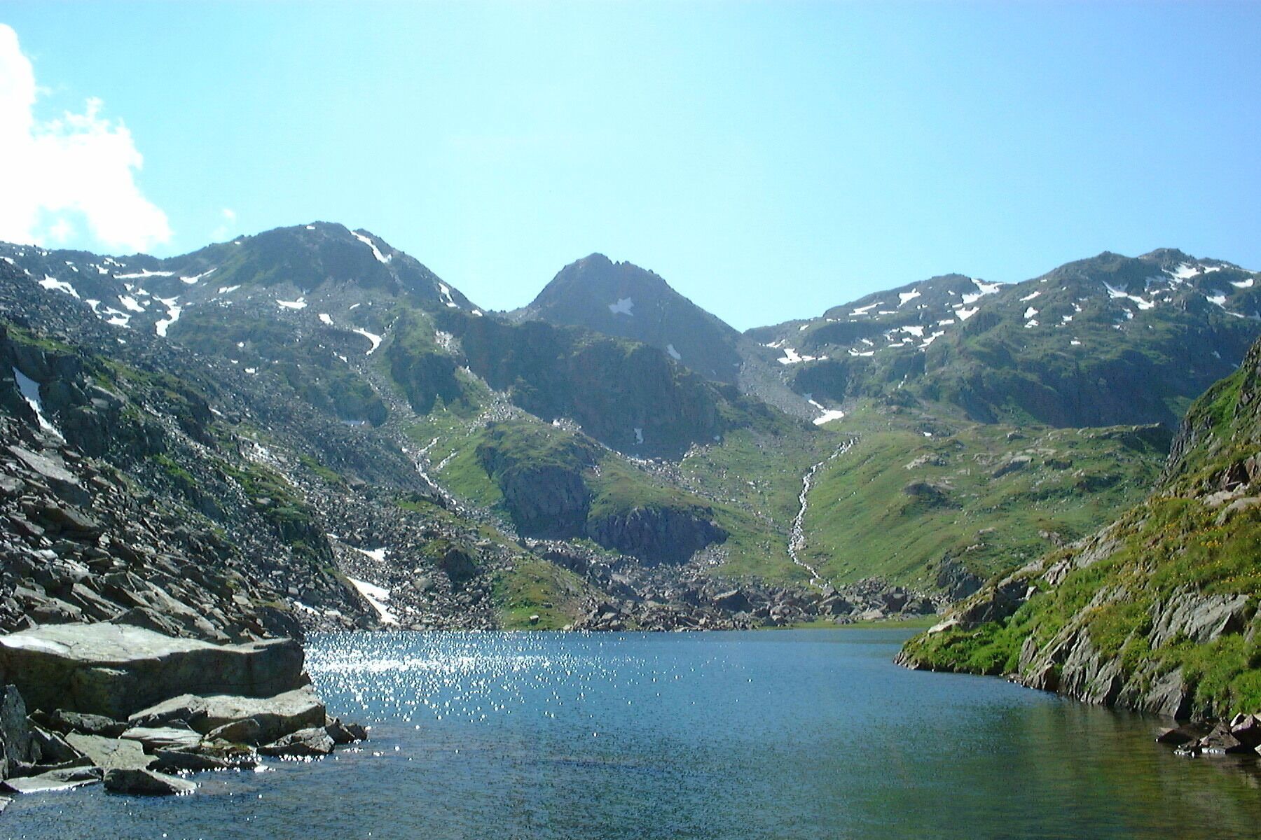 A mountainous landscape with a lake, rocky shores, and snow-capped peaks.