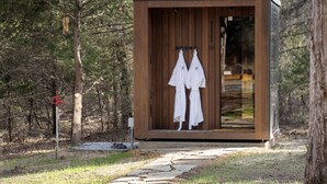 Une cabane en bois, dont la porte est ouverte, laissant apercevoir deux robes blanches suspendues à l’intérieur.