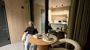 Un intérieur moderne avec une table ronde en bois, dressée pour deux personnes, une chaise confortable et un coin cuisine en arrière-plan.