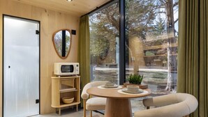 Une chambre moderne avec une porte en bois, un four à micro-ondes, une table ronde avec des chaises et une grande fenêtre donnant sur des arbres.