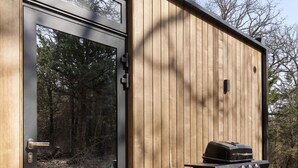 Una estructura de madera con puerta corredera, una parrilla para barbacoa y un felpudo.
