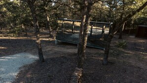 Un espacio al aire libre rústico con un banco de madera, rodeado de árboles y un camino de grava.