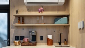 Una cocina moderna con aire acondicionado integrado, estantes de madera, una cafetera y un lavabo.