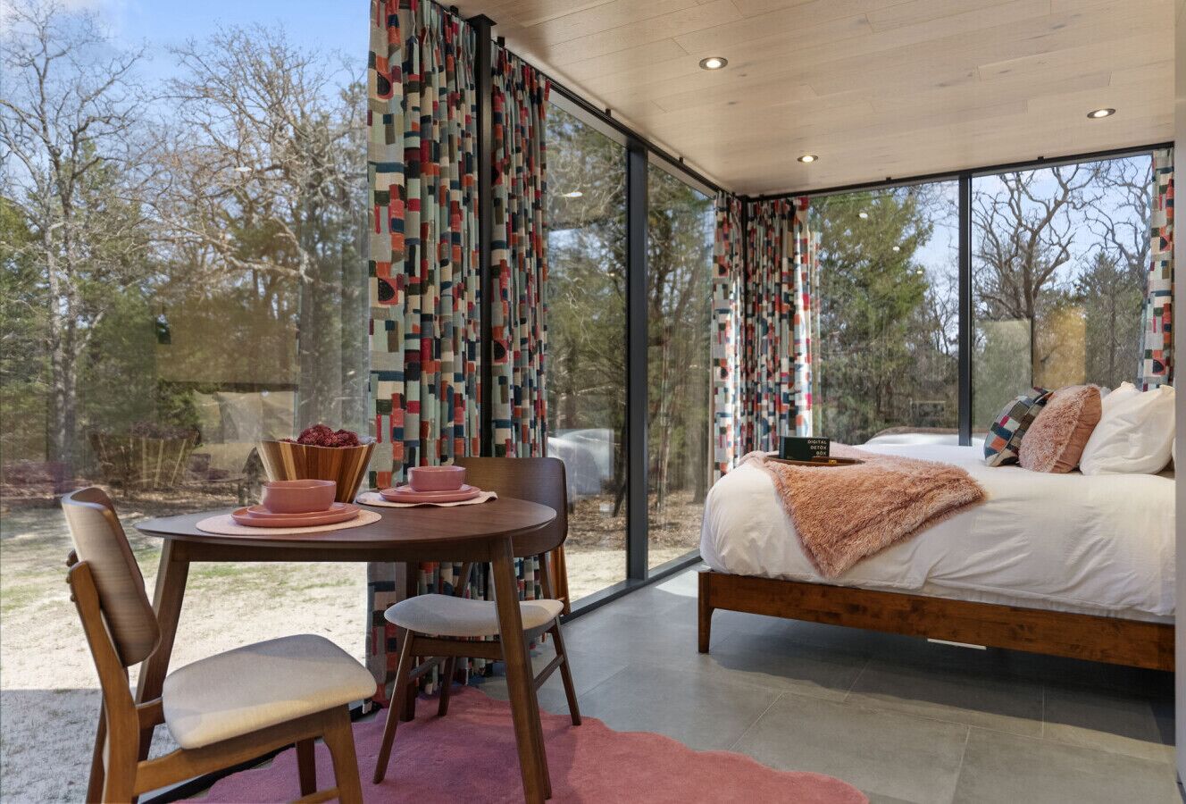 Quarto com cama grande, mesa de jantar com cadeiras e vista para o exterior.