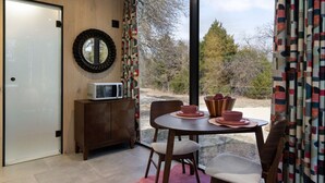 Un comedor con una mesa, sillas, microondas y un cuenco de fruta en el alféizar de una ventana.