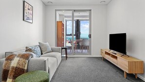 A modern living room with a grey sofa, a green ottoman, a wooden TV stand, and a large flat-screen TV. - Modern Haven w Sea and City Views nr Spark Arena (Auckland CBD)