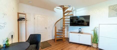 Una sala moderna con una escalera espiral de madera, un televisor de pantalla plana, una mesa de comedor y una zona de estar.
