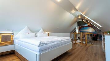 Un dormitorio moderno con una cama grande, suelo de madera y techo inclinado con iluminación integrada.