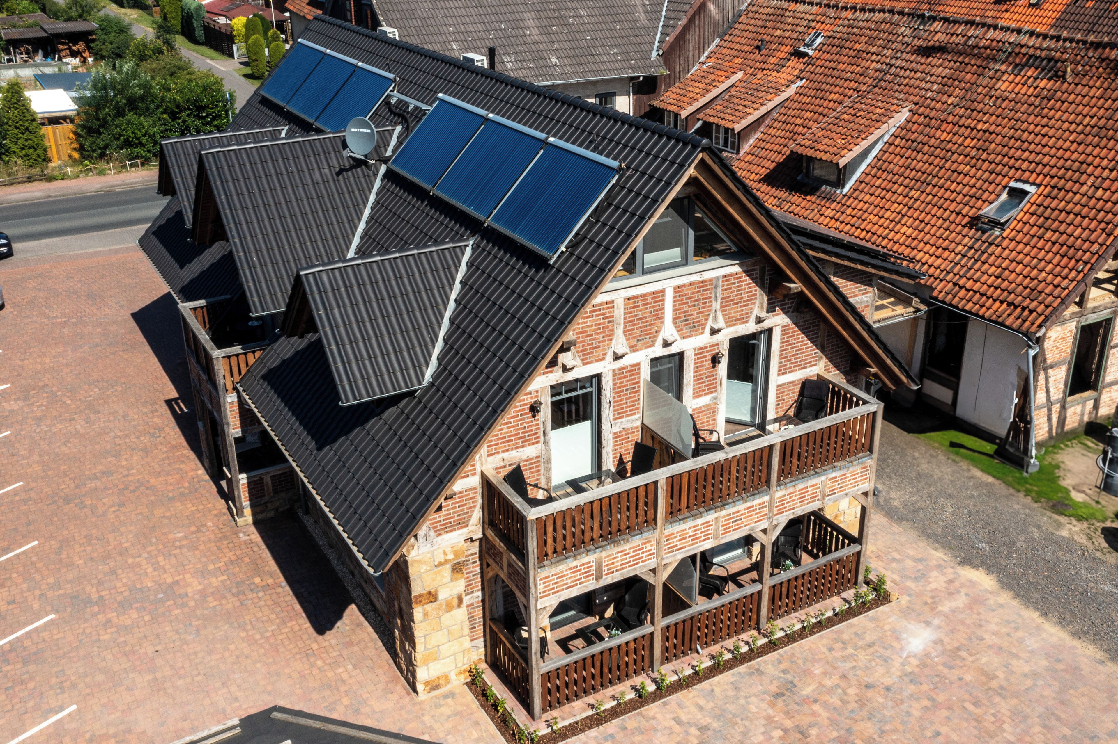 A two-story building with a sloped roof, solar panels, and a balcony with outdoor seating.