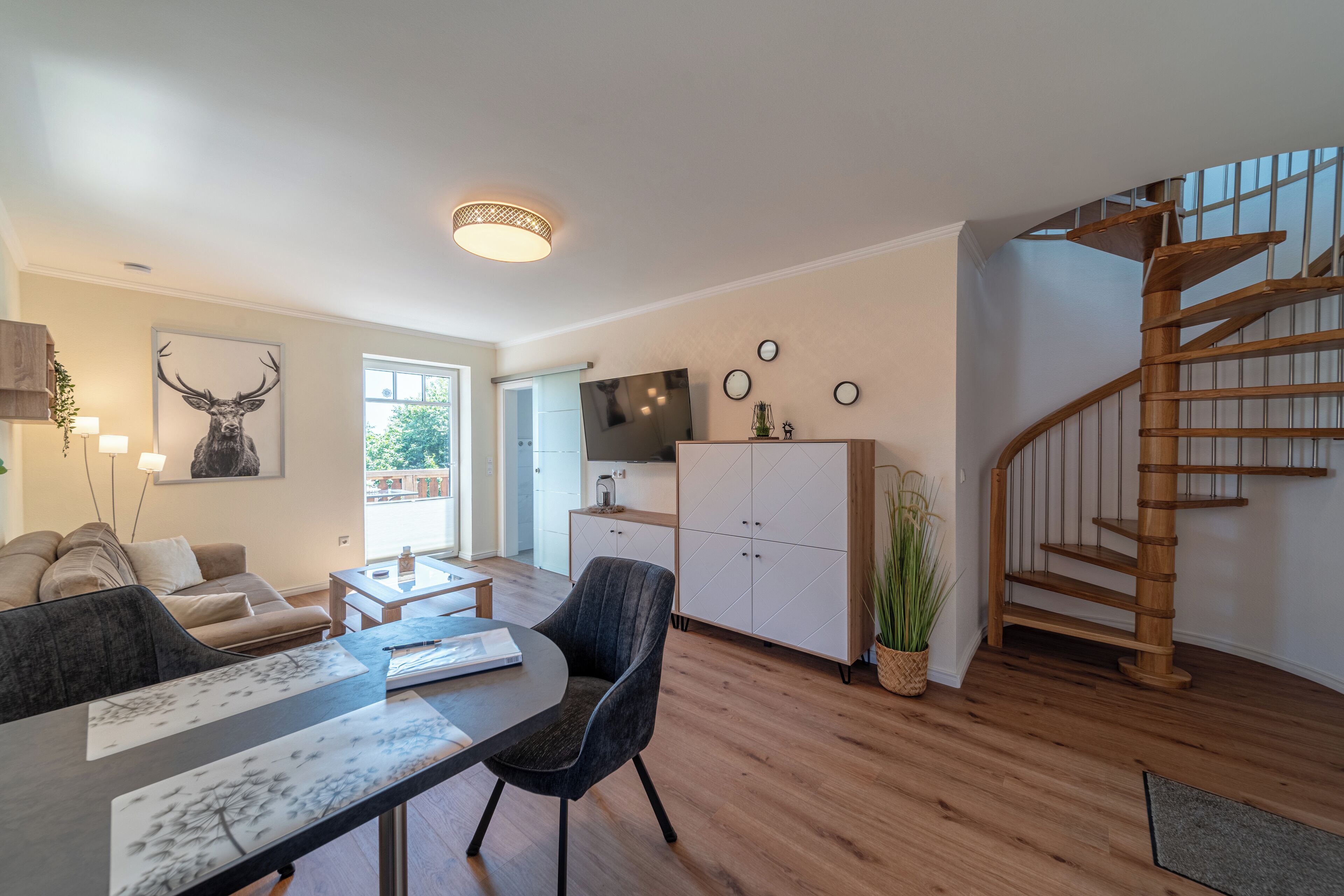 A modern living room with a dining area, a kitchen, and a wooden staircase.