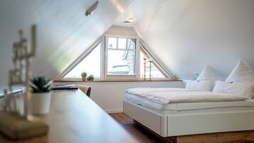A bedroom with a sloped ceiling, a bed, a desk, and a window with a view of the outside.