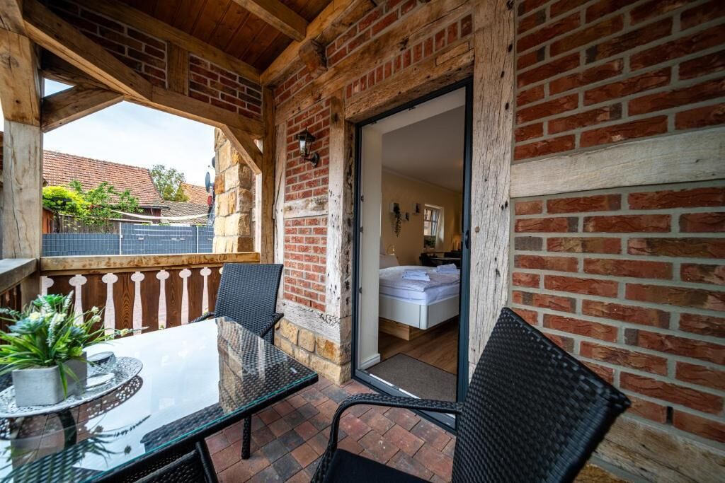 Een balkon met een glazen tafel en stoelen, een bakstenen muur en uitzicht op een tuin en gebouwen.