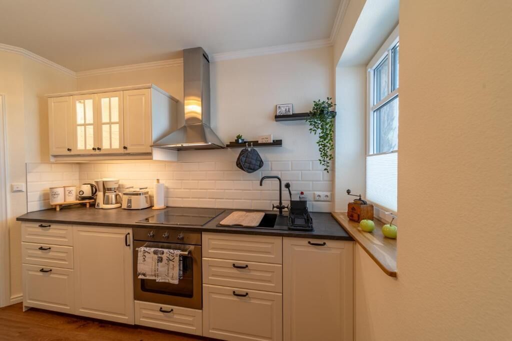 A kitchen with white cabinetry, a stainless steel range hood, a sink, and a window with a plant on the windowsill.