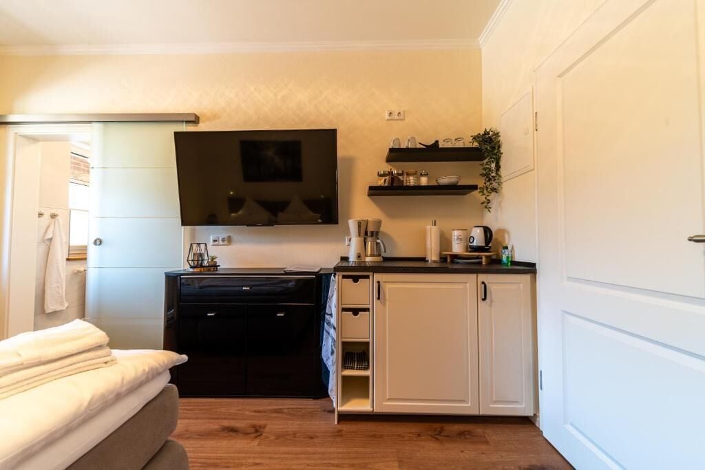 Una cocina compacta con un refrigerador negro, gabinetes blancos, un microondas y una cafetera.