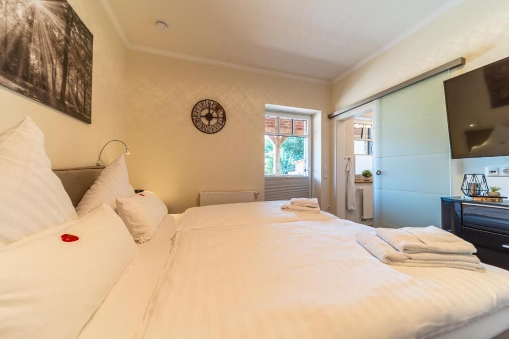 Une chambre d’hôtel avec un grand lit, une horloge au mur et un téléviseur sur le côté droit.