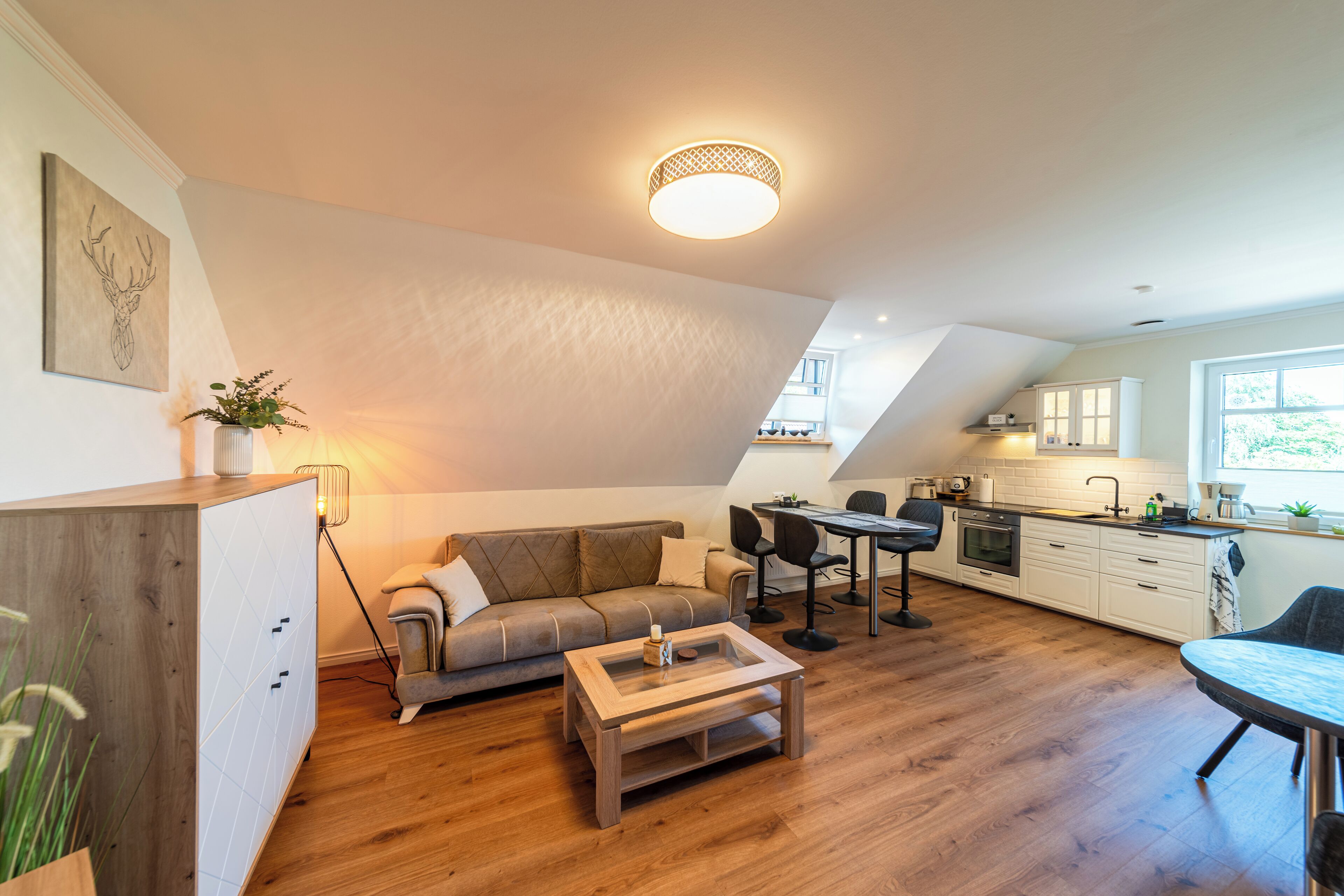 Un moderno espacio tipo loft con piso de madera, un sofá, una mesa de centro, un comedor y una cocina con armarios blancos.