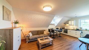Un moderno espacio tipo loft con piso de madera, un sofá, una mesa de centro, un comedor y una cocina con armarios blancos.
