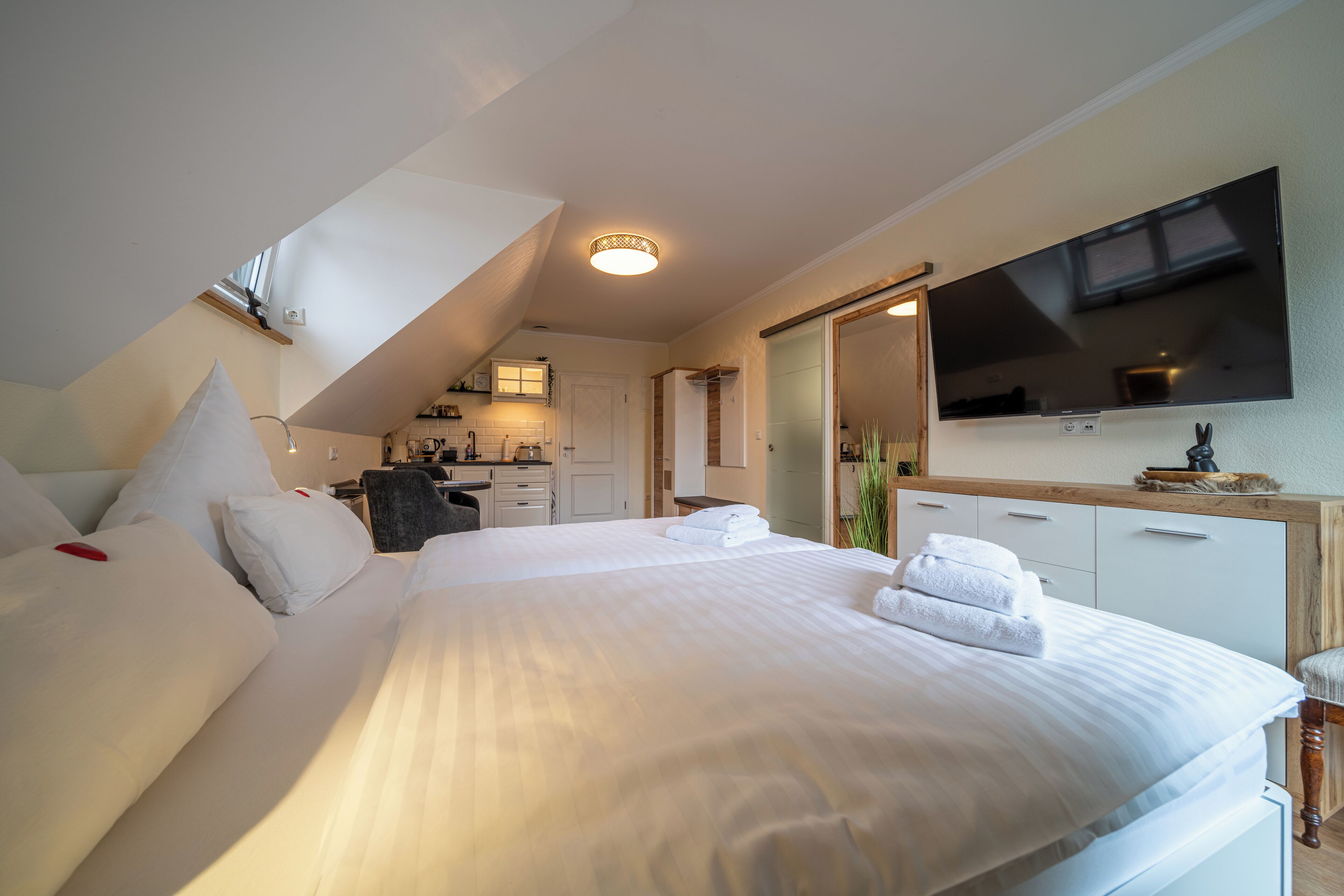 Una camera d'albergo con un letto grande, una televisione a schermo piatto fissata al muro e un angolo cottura sullo sfondo.