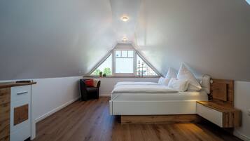 Un dormitorio con techo inclinado, una cama, una mesita de noche, un aparador y una ventana con vistas a la vegetación.