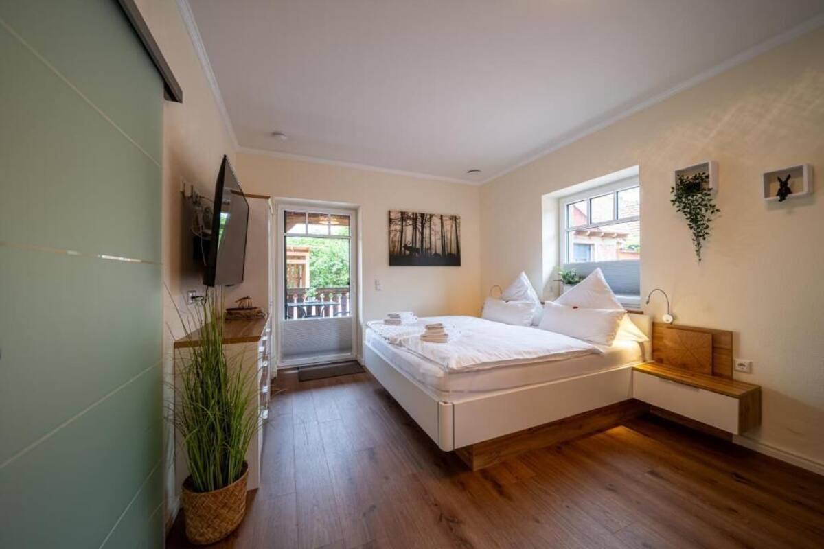 A bedroom with a bed, bedside table, lamp, and a potted plant.